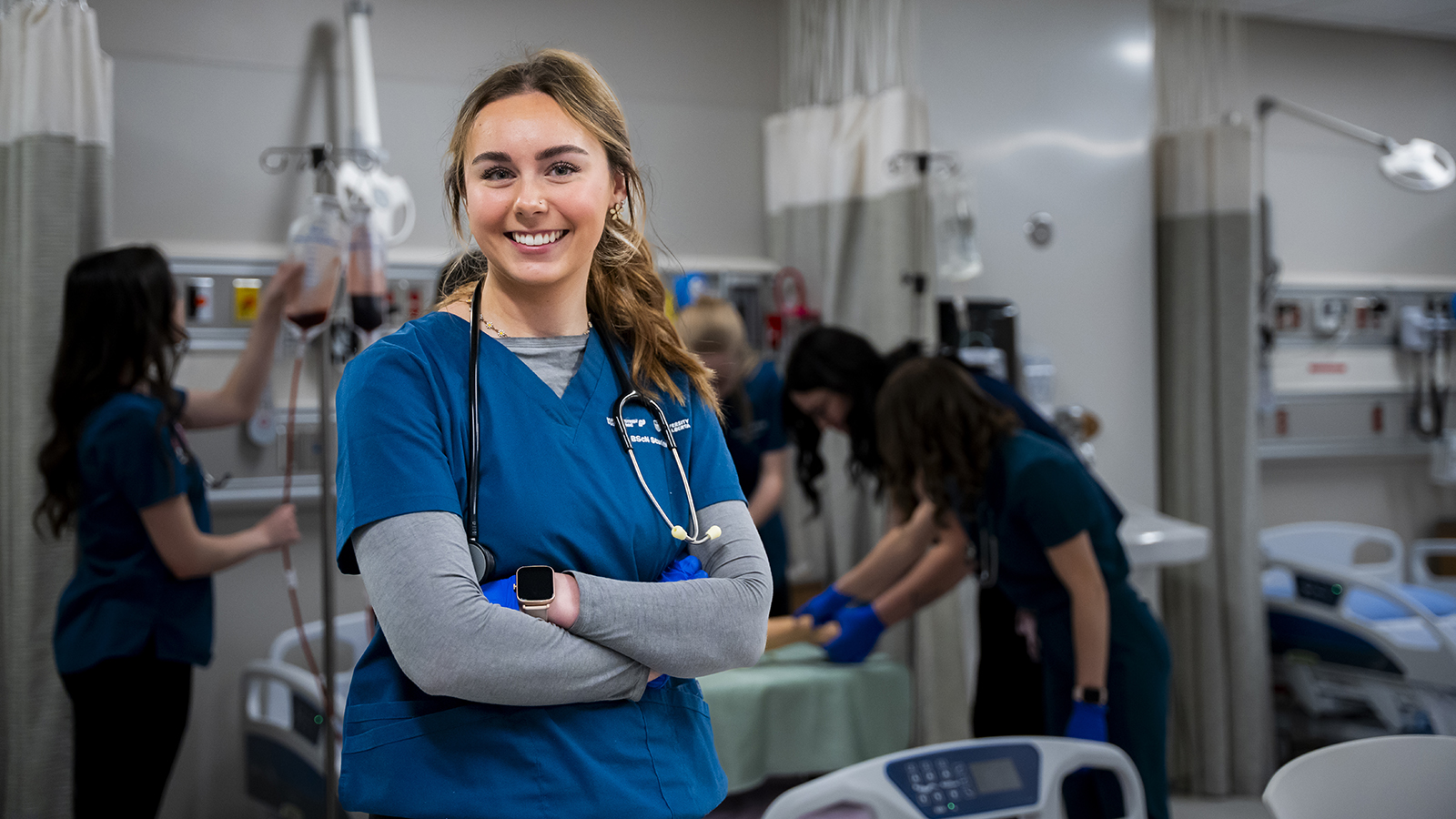 Nursing student in scrubs with a stethoscope around her neck in the simulation lab