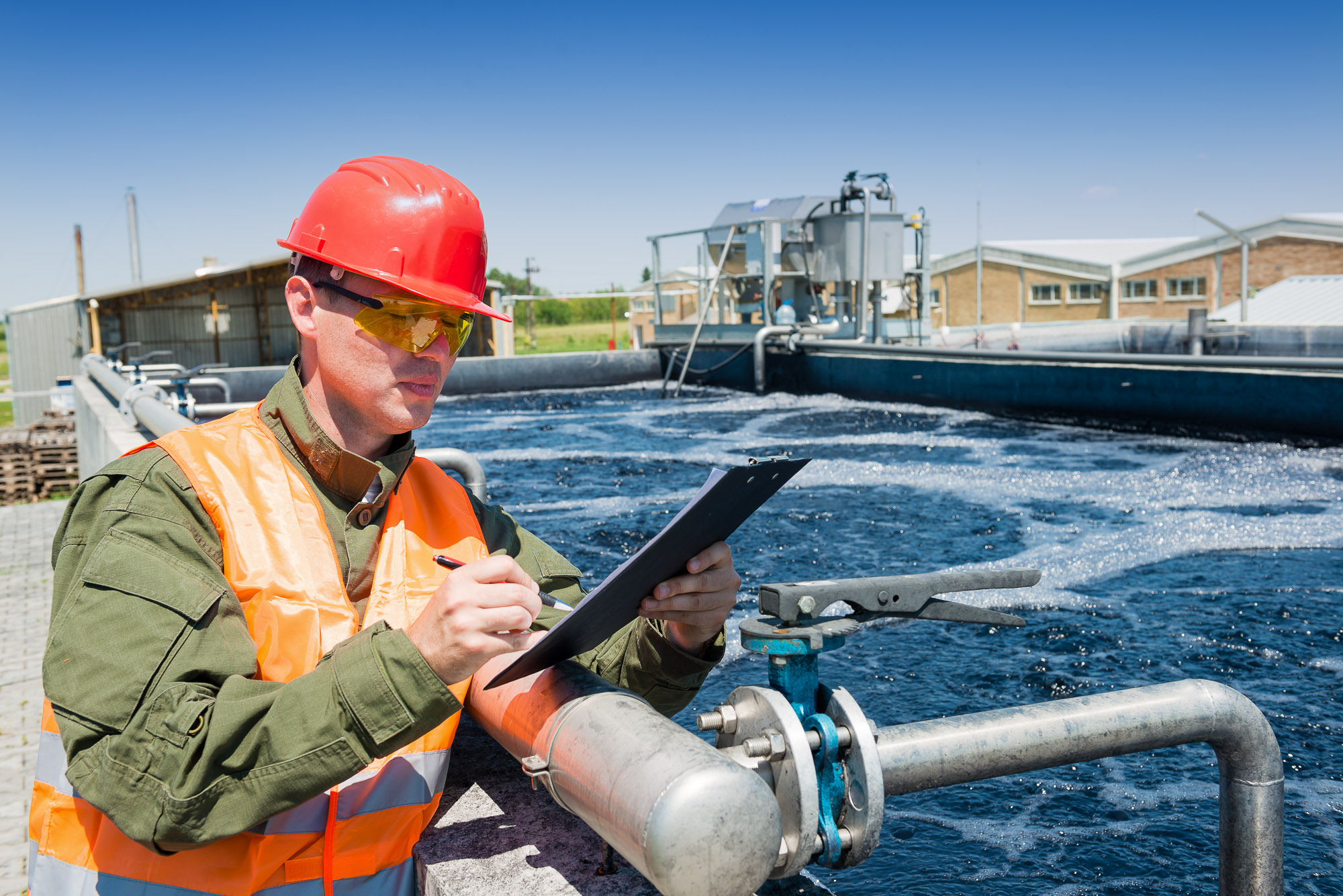 A technician with a clipboard monitoring the quality of water at a waste water treatment plant.