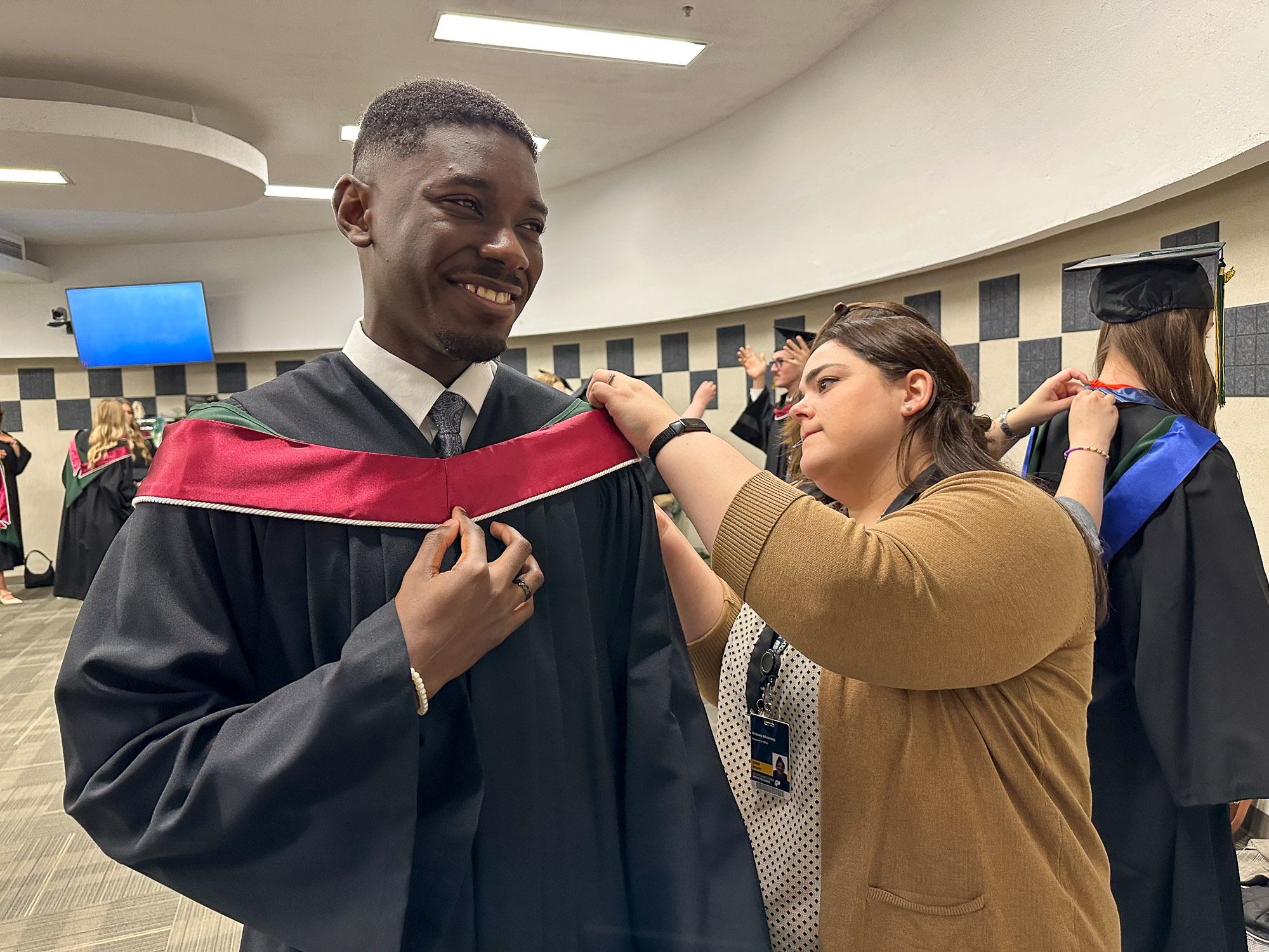 2025 Valedictorian Clinton Owusu smiles while receiving assistance gowning up before the Convocation ceremony