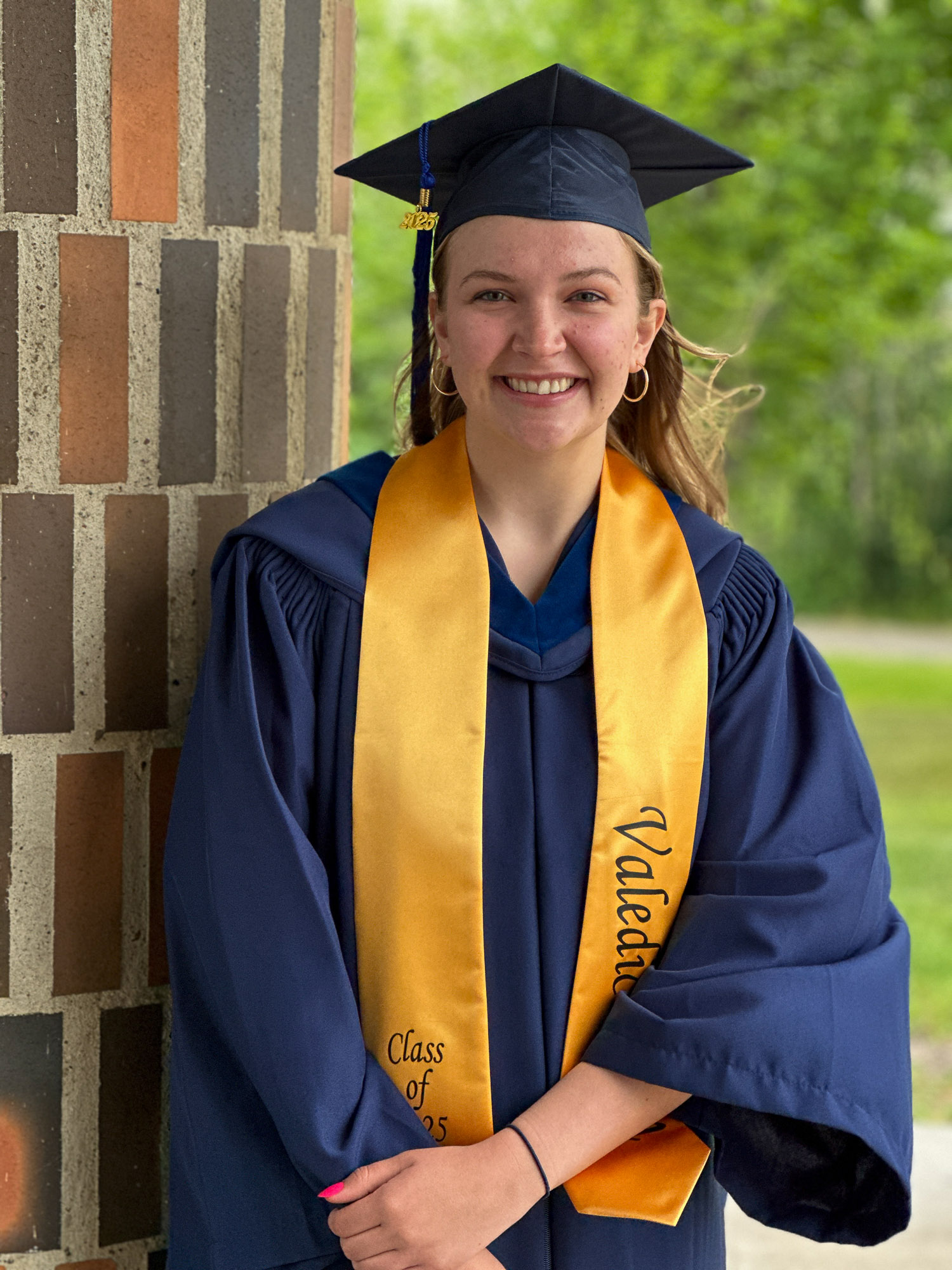 Valedictorian, Grace Larson happily posing in her gown and cap with Valedictorian sash draped around her neck