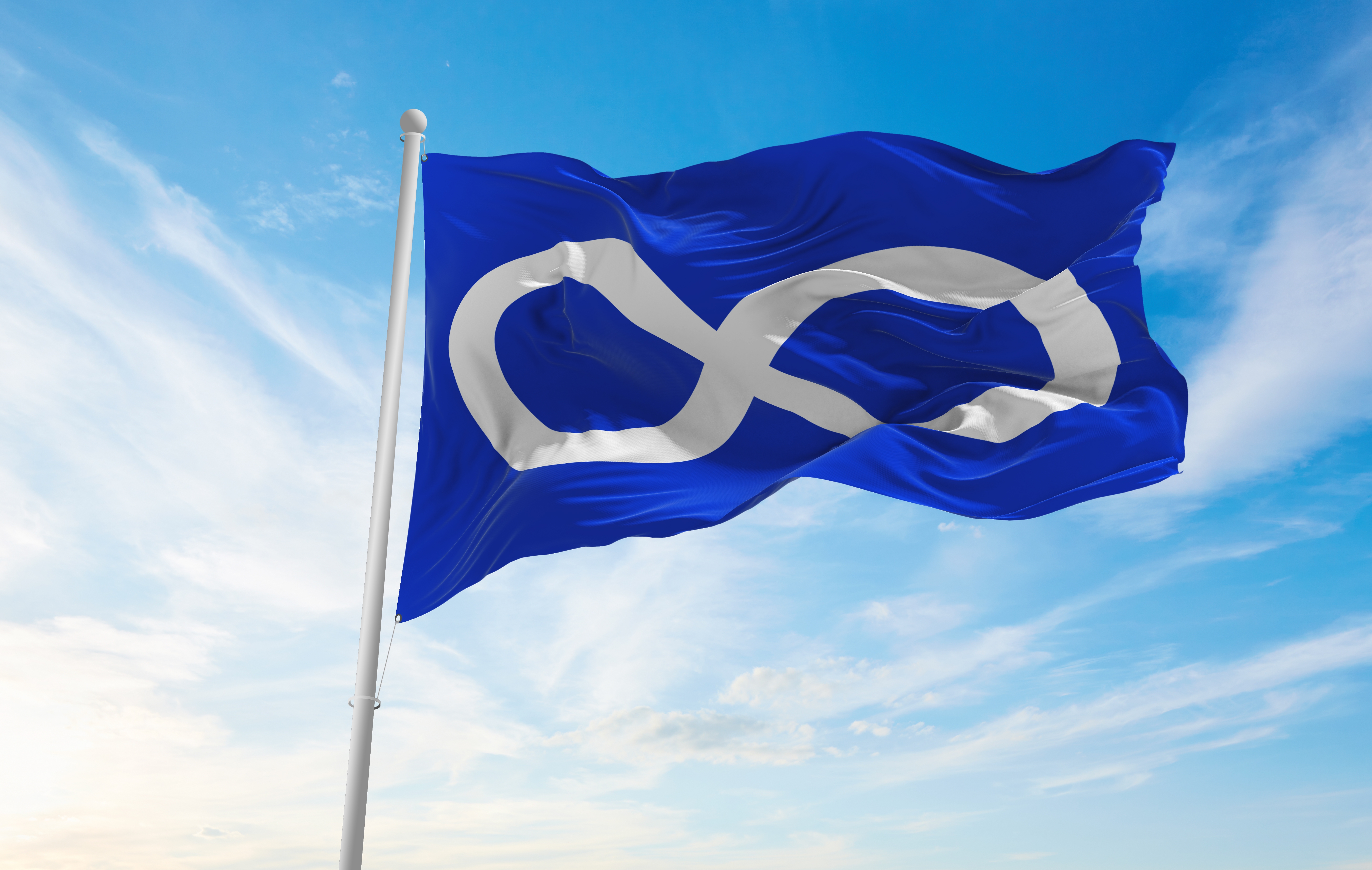 The Métis flag blowing in the wind set against a blue sky with clouds