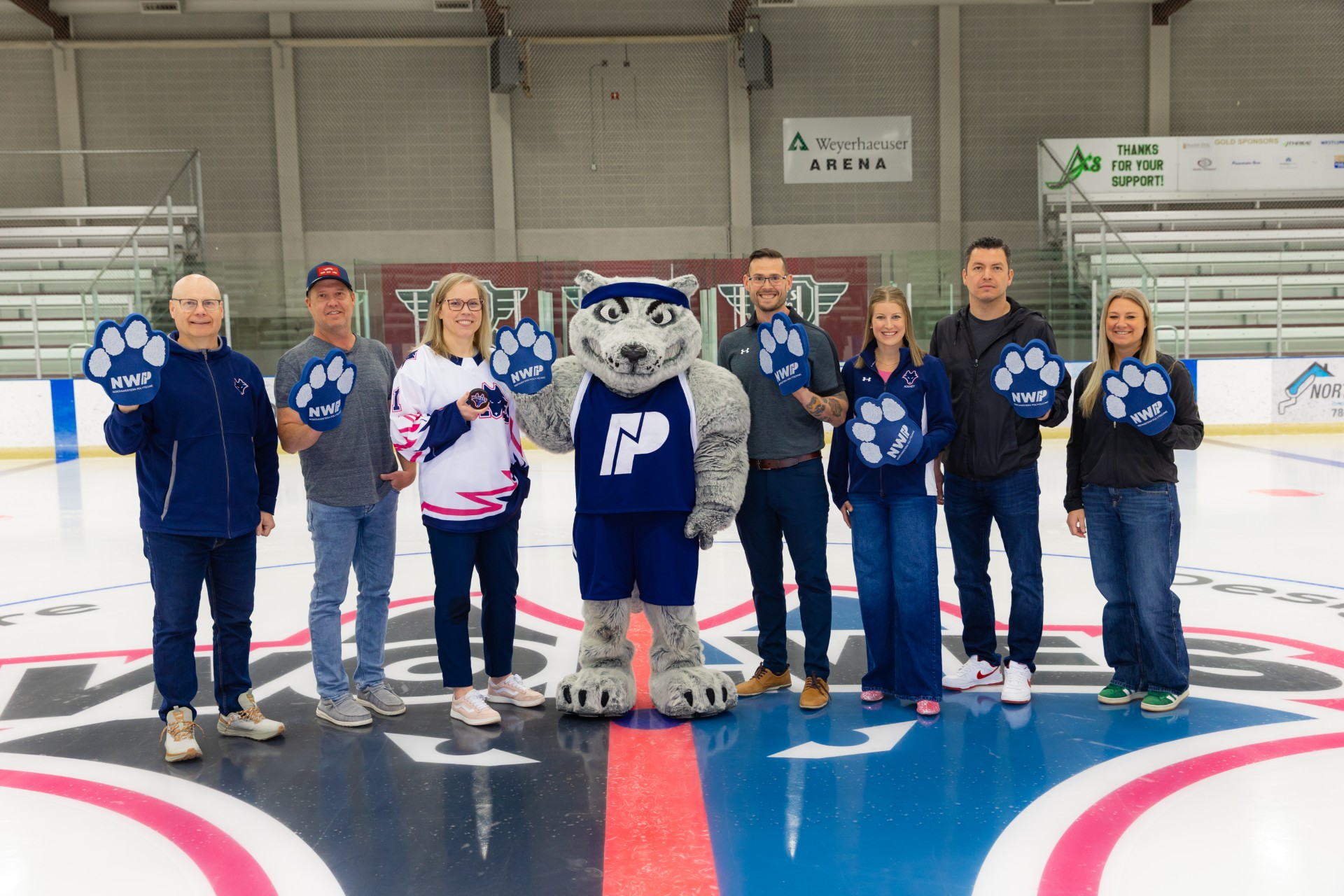 NWP and PCFAC leadership standing on centre ice at the Design Works arena waving giant foam wolf paws