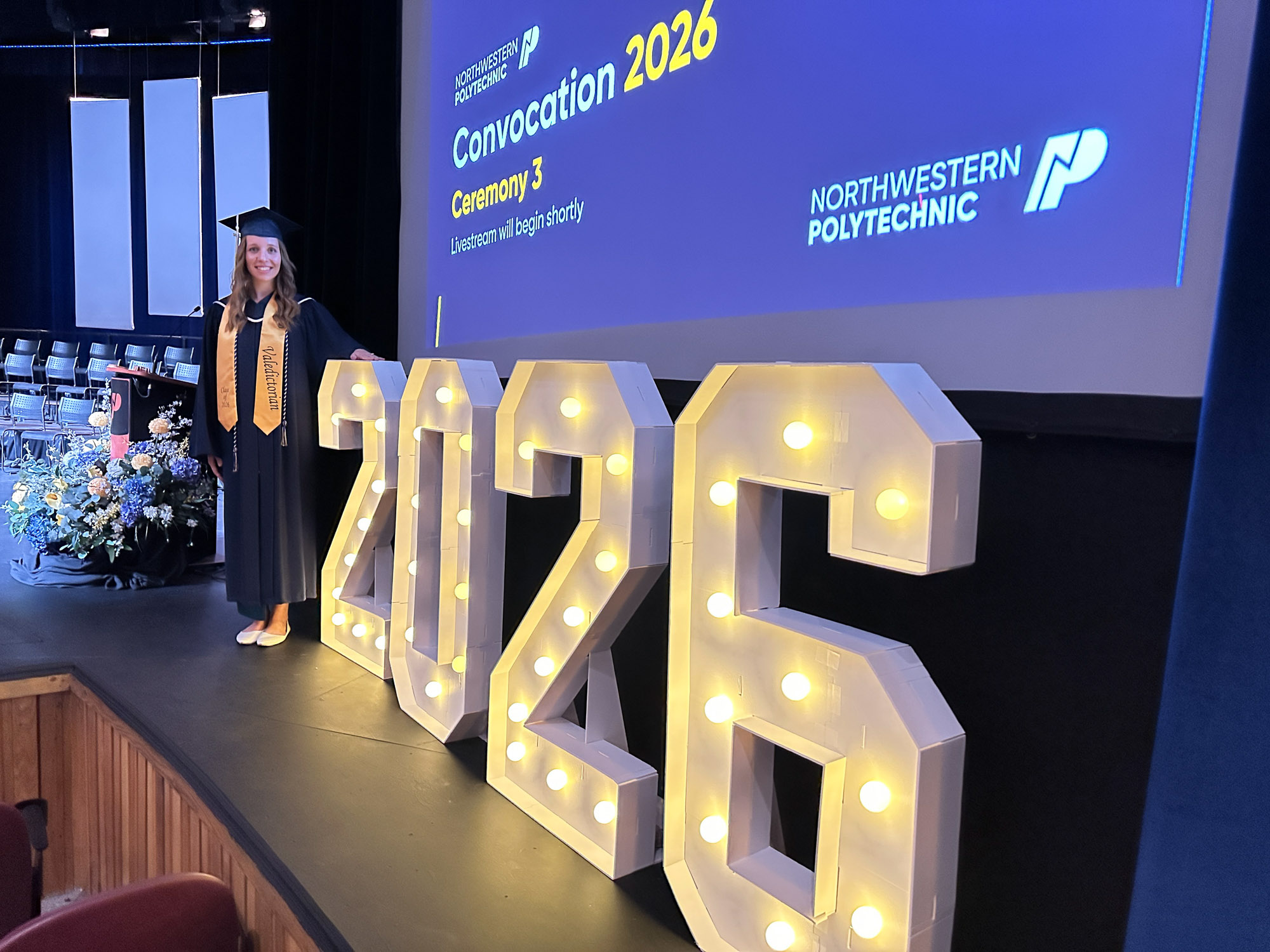 Valedictorian, Courtney Dyck in front of an illuminated 2026 sign