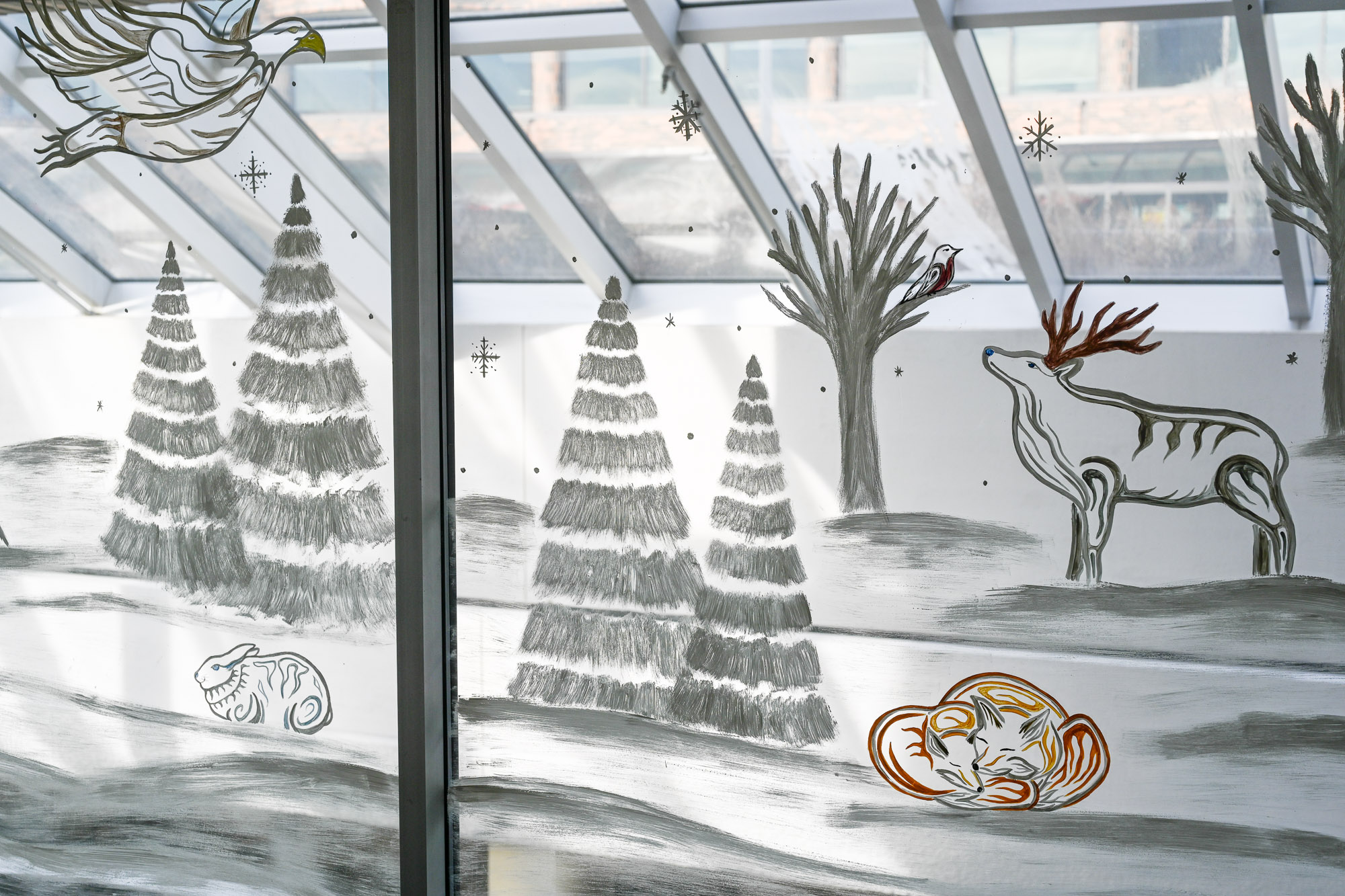 An Indigenous mural of a winter scene featuring an elk, a curled up fox and pup, rabbit, flying eagle, and snow covered trees