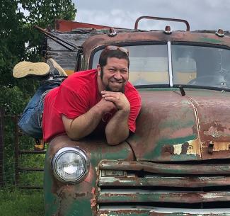 Vet tech instructor Chris Mizzi posing on the hood of an abandoned antique pickup truck