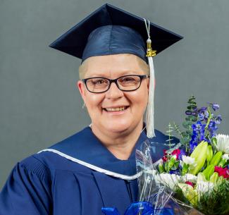 NWP Practical Nurse diploma graduate, Charity Bettenson wearing her graduation regalia and holding a bunch of flowers