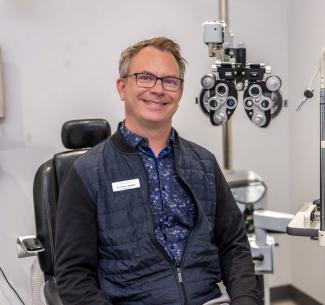 Dr Jeremy Begalke, optometrist, seated in his treatment room beside a phoropter