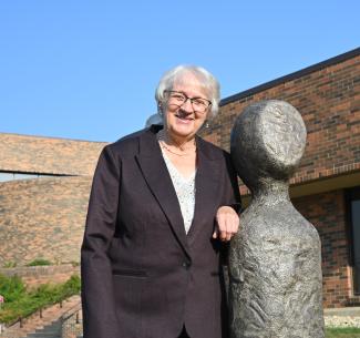 Helena Peters Mulligan standing beside one of her sculptures that stand at the main entrance of the Grande Prairie campus