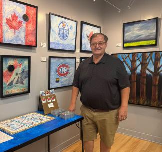 NWP alumni and artist Carmen Haakstad poses proudly alonside a few of his paintings at a recent exhibition.