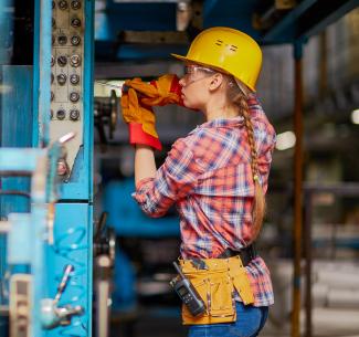 A skilled trades technician wearing safety gear works on a piece of equipment