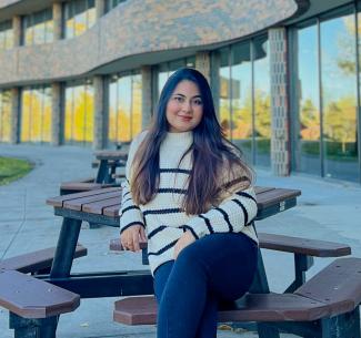 Busayna sitting on a bench on a clear summers aday with the NWP Cardinal building in the background