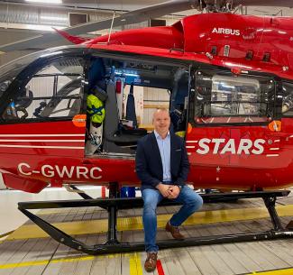 Shawn Shmyr seated at the entrance to the cabin of a bright red STARS helicopter