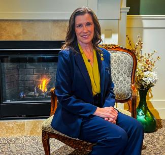Smartly dressed NWP Alumni, Eunice Friesen seated on an ornate chair in front of a warm and inviting fireplace