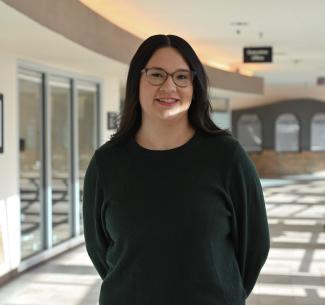 Jai Lin Mark, NWP alumna, posing in the E-wing corridor at NWP with warm sunshine streaming through the windows behind her