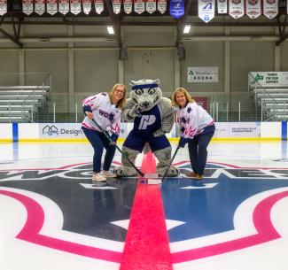 Mayor Clayton and NWP President Vanessa Sheane holding hockey sticks at centre ice with Farley the mascot