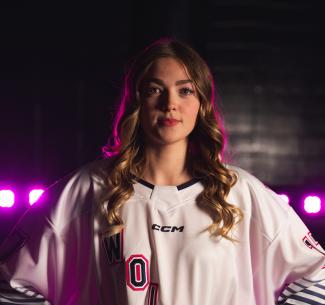 Jaida Klimach posing in her team jersey. Pink lights shine brightly behind her. 