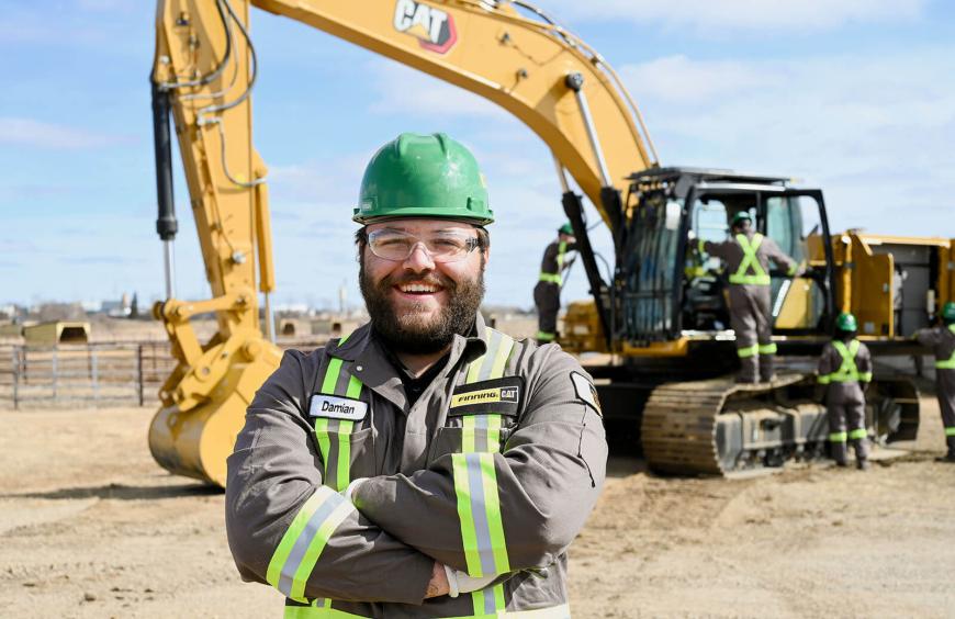Student wearing a hard had posing in front of earth moving equipment