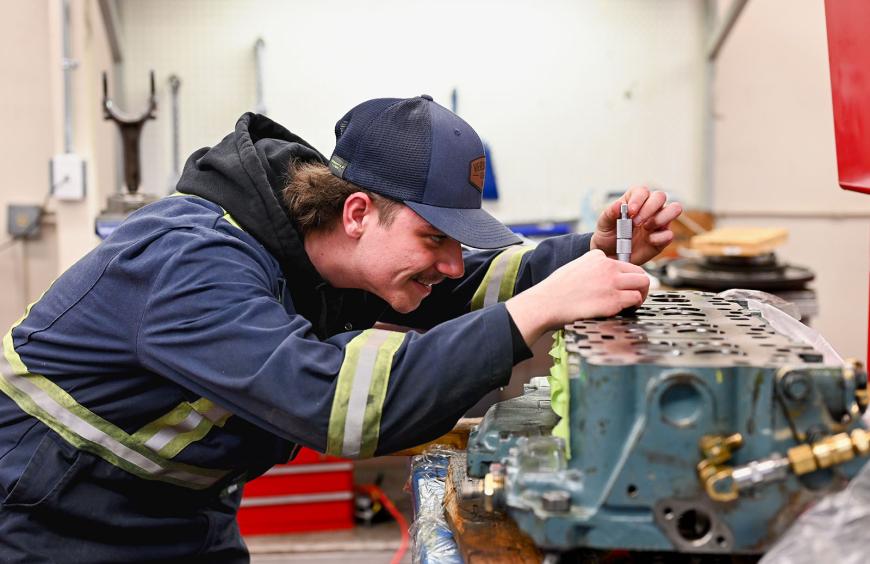 A student skillfully working on an engine for a piece of heavy equipment in a busy workshop.