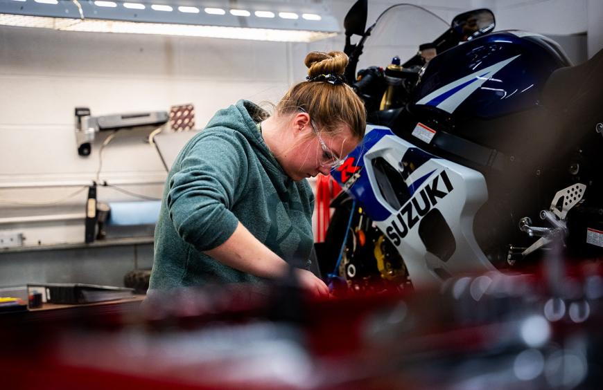 An NWP student focused on repairing a motorcycle in a well equipped workshop.