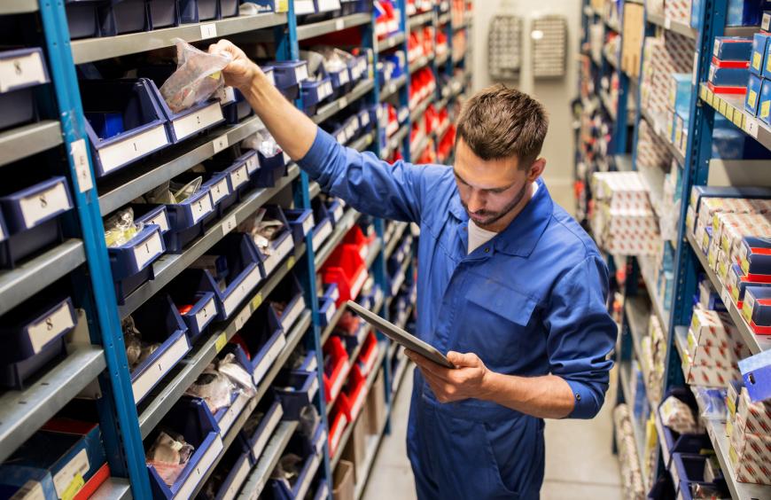 Parts technician reading a list off a clipboard and reaching into a bin of parts
