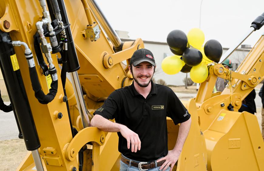Cheerful trades student standing in front of a large piece of yellow excavation equipment