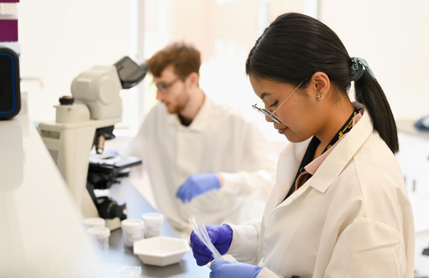 Scientist in a white lab coat using a pipette to perform an experiment.