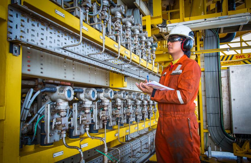 A worker wearing a hard hat and coveralls taking readings in a power plant