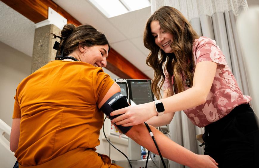 A practical nursing student measuring the blood pressure of a fellow student in the nursing simulation lab