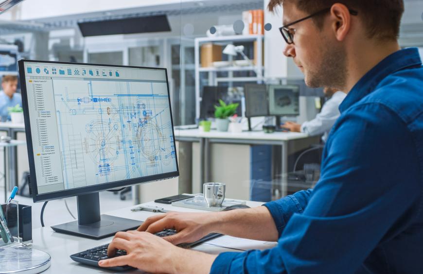 An engineers sitting at a computer working on blueprints.