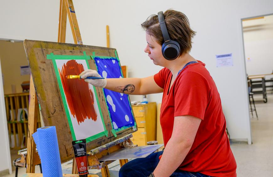 Art student sitting at an easel paining a brightly coloured picture