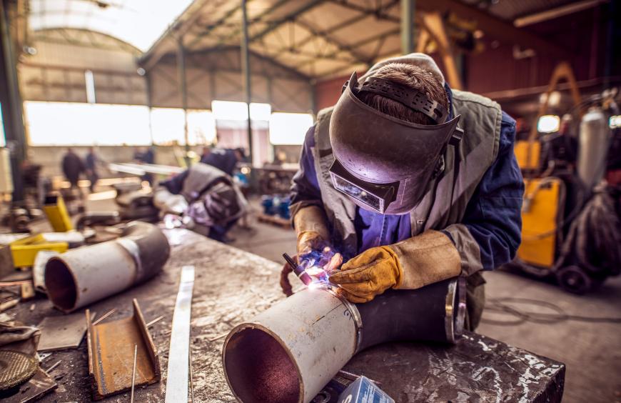Pipefitter welding a large pipe in a busy workshop