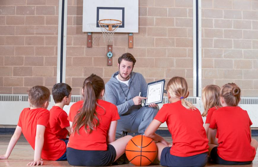 Phys Ed teacher in the gym addressing a group of school children