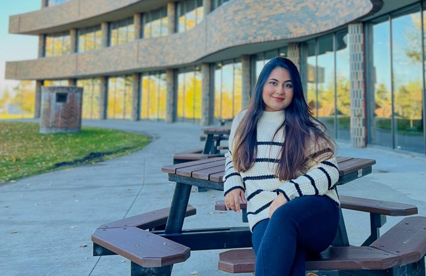 Busayna sitting on a bench on a clear summers aday with the NWP Cardinal building in the background