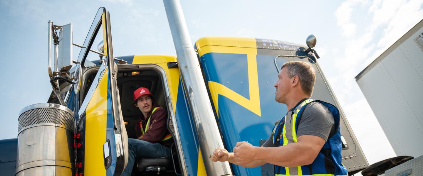 Student sitting in the cab of a semi-truck receiving instruction from a driving instructor