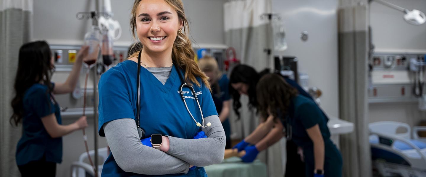 Nursing student in scrubs with a stethoscope around her neck in the simulation lab