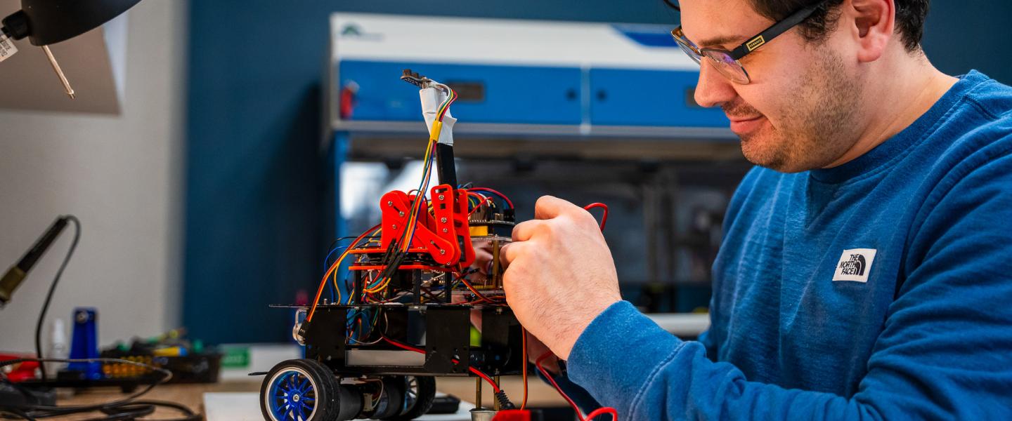 A computing science student working intently on a robotic gadget in the lab.