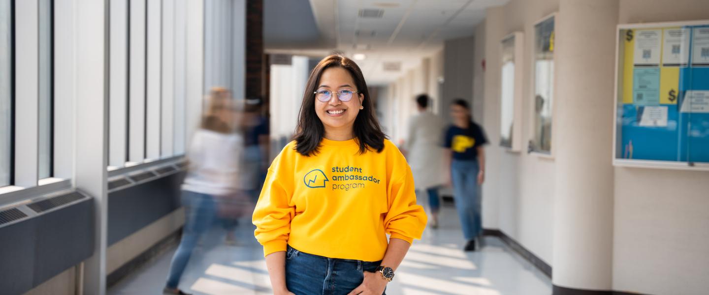 Happy student standing in a hallway on GP campus wearing a bright yellow sweatshirt 