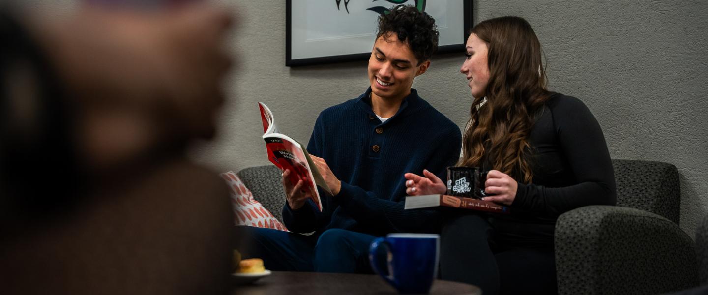 Two students sitting on a couch reading from a text book
