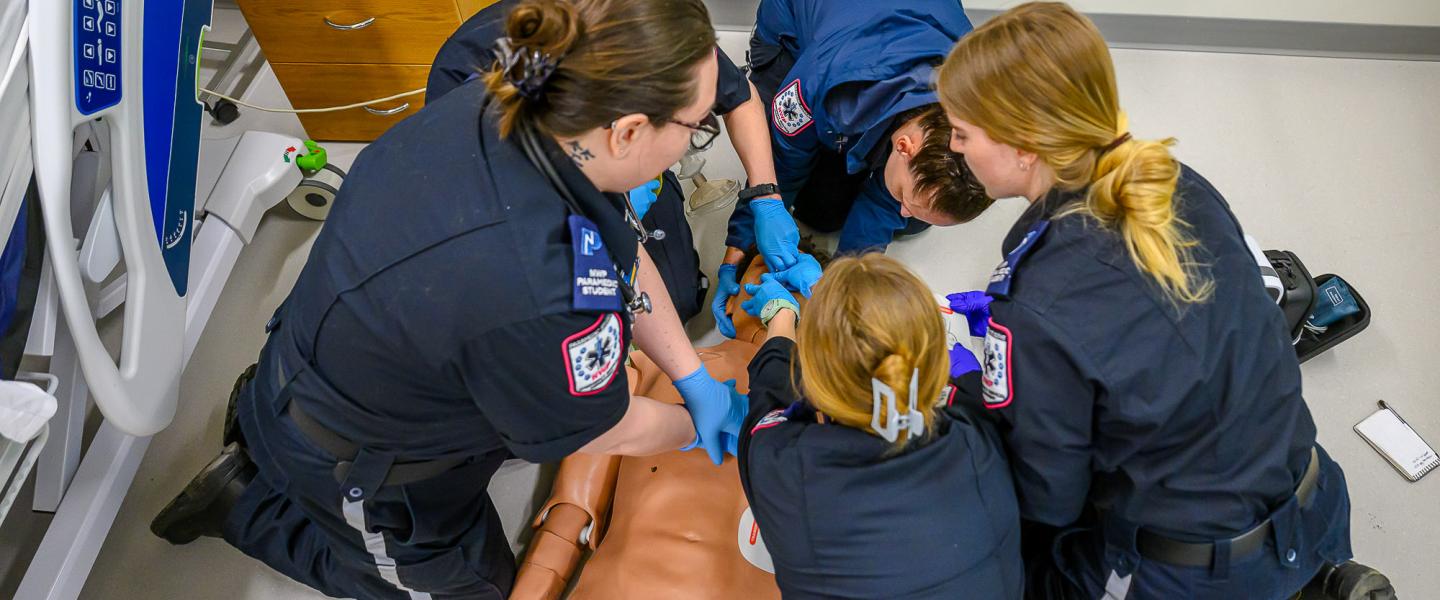 A group of paramedic students surrounding a dummy in the simulation lab