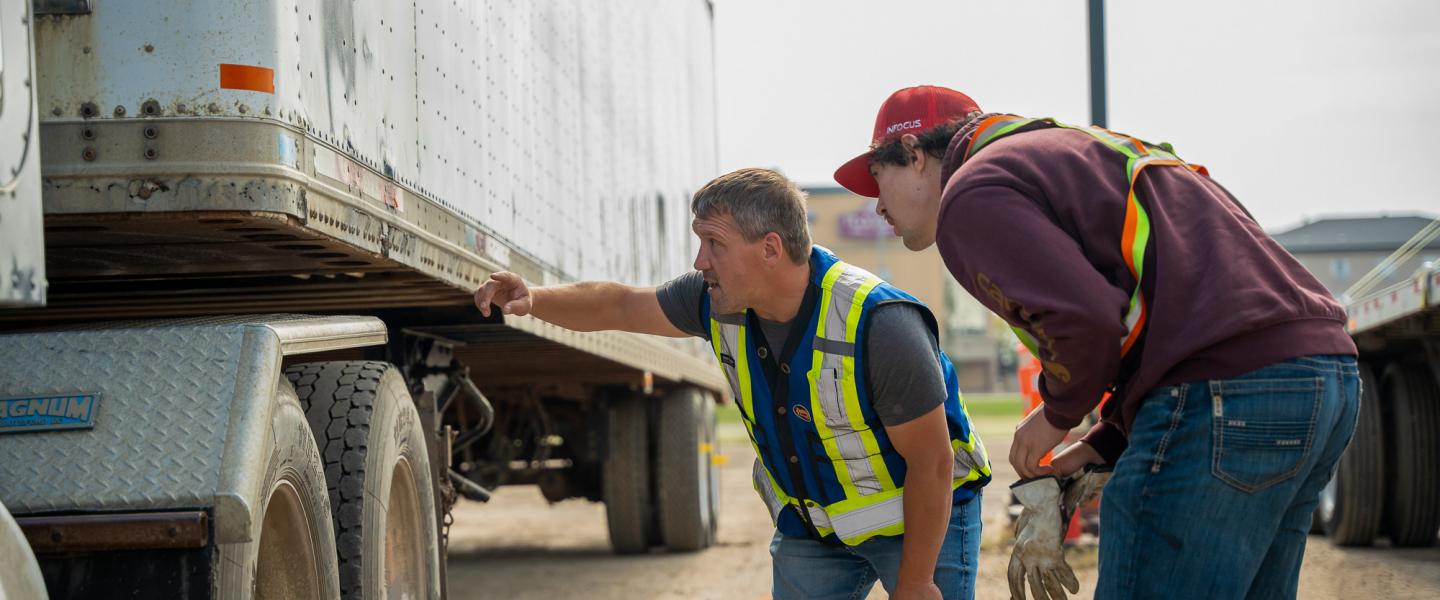 Driver training instructor and student inspecting the undercarriage of a semi truck and trailer.