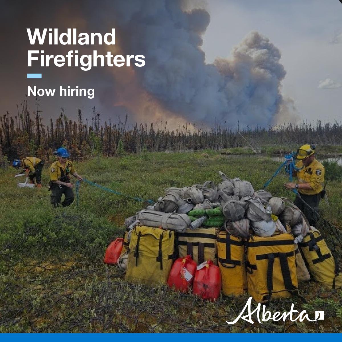 Firefighters in the bush preparing their gear in front of a large plume of smoke in the distance behind
