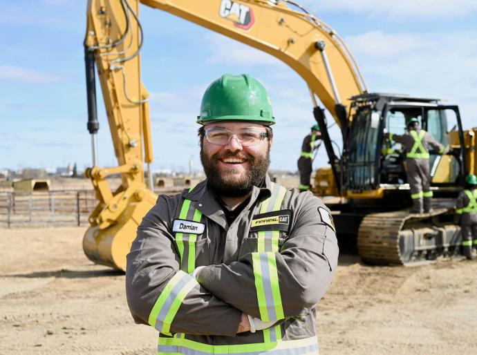 Student wearing a hard had posing in front of earth moving equipment