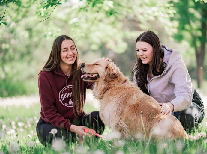 Students petting Mowgli the therapy dog outside on the grass under a tree