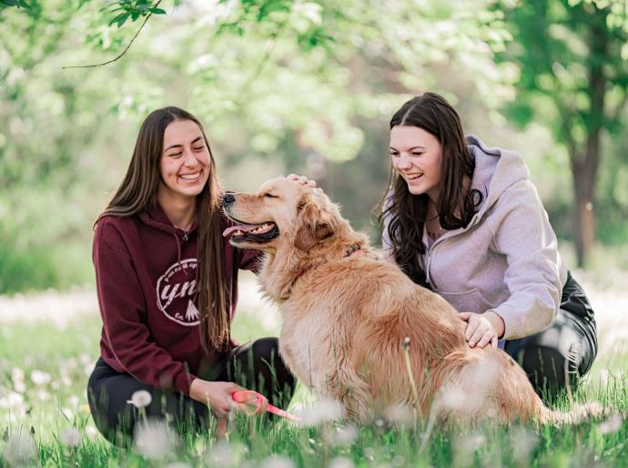 Students petting Mowgli the therapy dog outside on the grass under a tree
