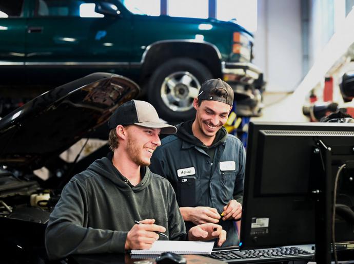 Automotive apprenticeship students interacting in a workshop with a vehicle in the background