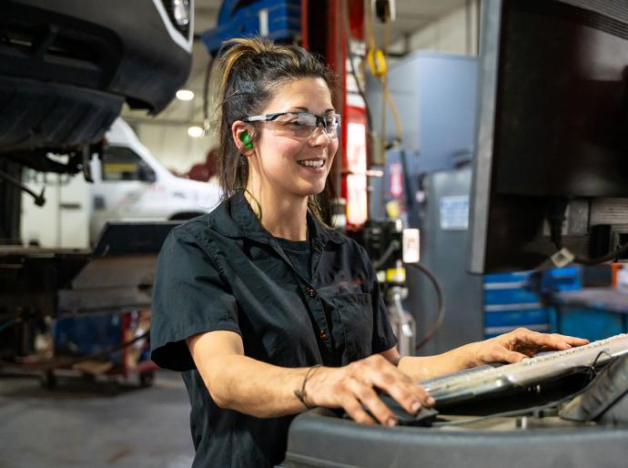 A women in an automotive shop searches for a part number on a computer, with a vehicle in the background.