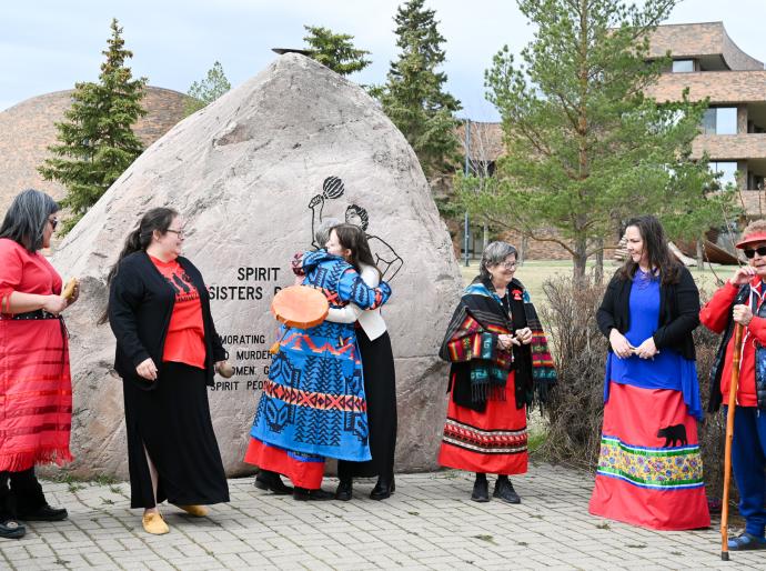 Attendees embrace on Red Dress Day in front of the Spirt Sisters Rock on Grande Prairie Campus.