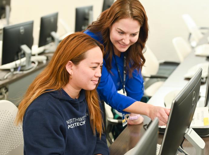 Instructor pointing at a computer screen and helping a smiling student.