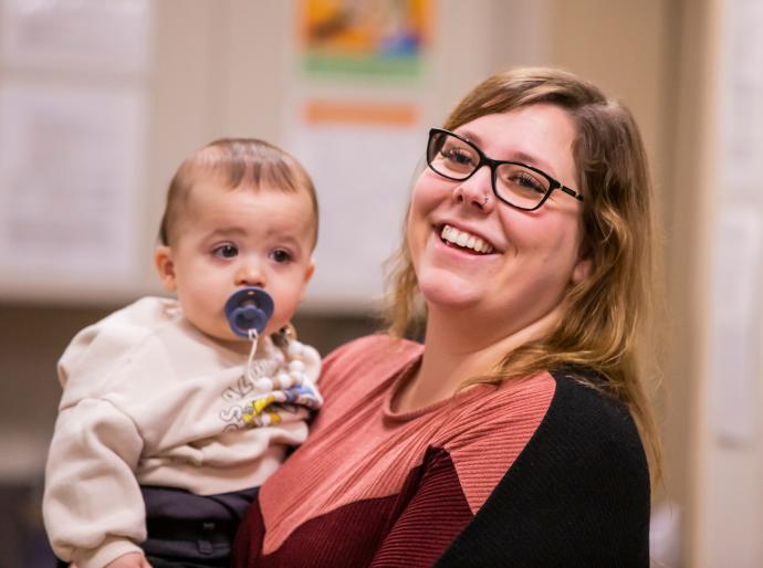 A cheerful daycare working smiling while holding an infant with a pacifier.