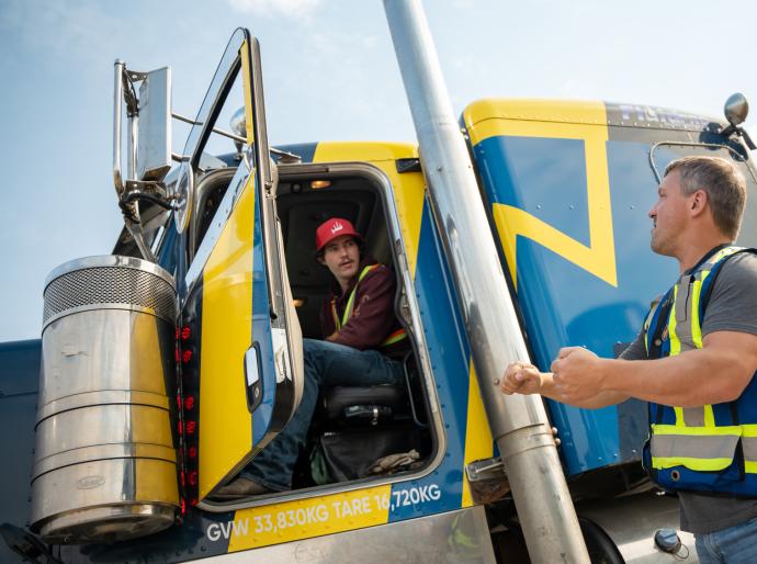 Student sitting in the cab of a semi-truck receiving instruction from a driving instructor